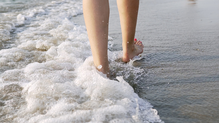 Following a barefoot female feet walking and splashing on sea water waves, cinematic steadicam shotの写真素材