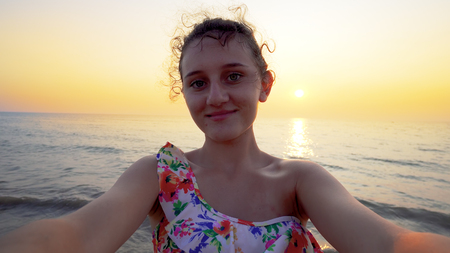 Beautiful teen in bikini makes funny selfie grimaces with summer sea sunset at backgroundの写真素材