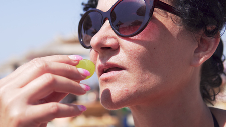 Close up portrait of a woman with glasses eating grape on beachの写真素材
