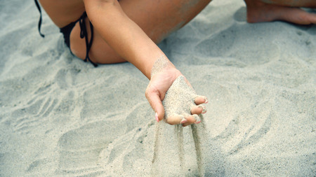 Sand pours out of fashion model hands sitting on beachの写真素材