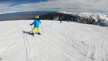 active child kid with safety helmet, goggles and poles ski on slopeの写真素材