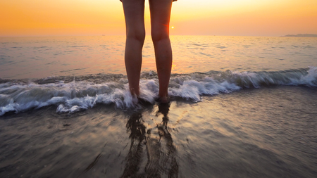 Woman feet splashed by sea waves on beach sunset. Calm serene relaxing scene of ocean water splashing on feet on beautiful beachの写真素材