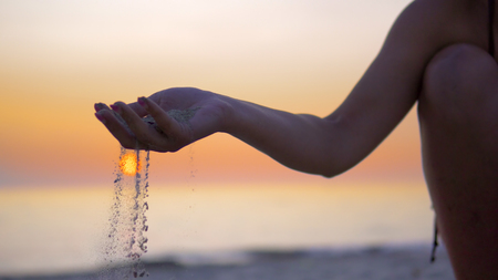Silhouette hand releasing dropping sand. Sand flowing through the hands against orange ocean sunset. Summer beach holiday vacation conceptの写真素材