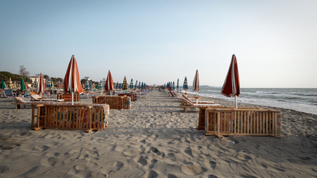 Empty beach in the seaside resort with folded sun loungers and umbrellas on a background of sunrise skyの写真素材