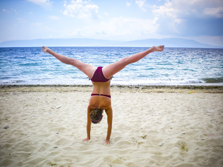 Cheerful caucasian young woman performing gymnastic working out in beachの写真素材