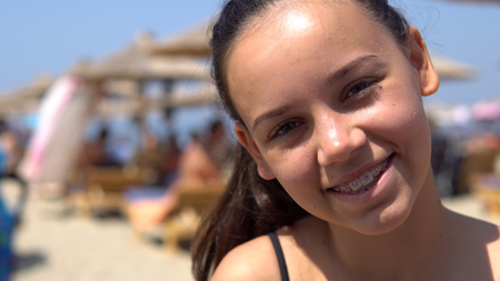 Beautiful happy teen girl with tooth braces smiling to camera sitting on beach during summer vacationの写真素材