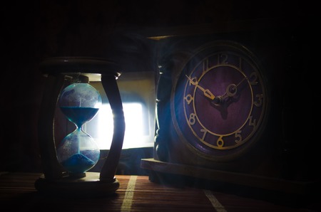 Time concept. Silhouette of Hourglass clock and old vintage wood clock with arrow and smoke on dark...