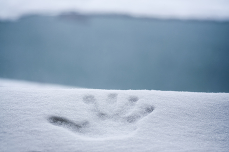 Perfect hand print in fresh snow, with blurred background of lake and mountainの写真素材