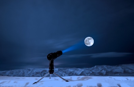 Surreal concept. Lamp on tripod pointed light to the moon with blurred background of mountains with snowの写真素材