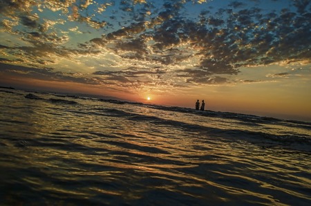 Young girls in warm water at sunset. Gorgeous colors in the sky and the sea. People standing and watching to sunset at Caspian sea. Baku, Azerbaijan. Perfect shapes reflected in waterの写真素材