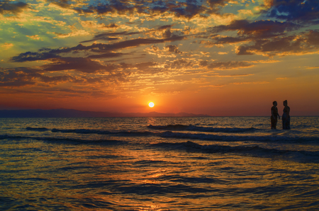 Young girls in warm water at sunset. Gorgeous colors in the sky and the sea. People standing and watching to sunset at Caspian sea. Baku, Azerbaijan. Perfect shapes reflected in waterの写真素材