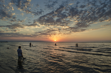 Young girls in warm water at sunset. Gorgeous colors in the sky and the sea. People standing and watching to sunset at Caspian sea. Baku, Azerbaijan. Perfect shapes reflected in waterの写真素材