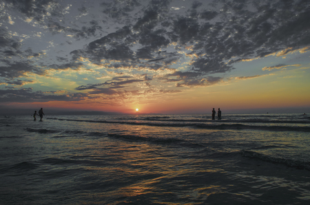 Young girls in warm water at sunset. Gorgeous colors in the sky and the sea. People standing and watching to sunset at Caspian sea. Baku, Azerbaijan. Perfect shapes reflected in waterの写真素材