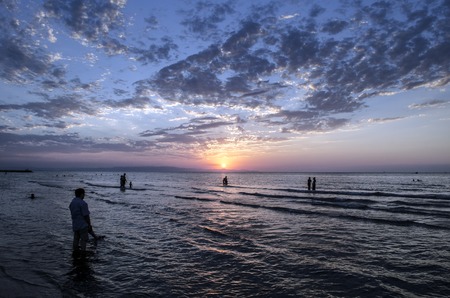 Young girls in warm water at sunset. Gorgeous colors in the sky and the sea. People standing and watching to sunset at Caspian sea. Baku, Azerbaijan. Perfect shapes reflected in waterの写真素材