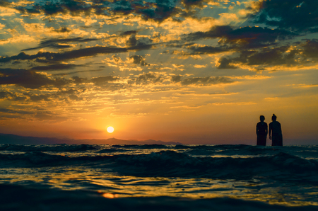 Young girls in warm water at sunset. Gorgeous colors in the sky and the sea. People standing and watching to sunset at Caspian sea. Baku, Azerbaijan. Perfect shapes reflected in waterの写真素材