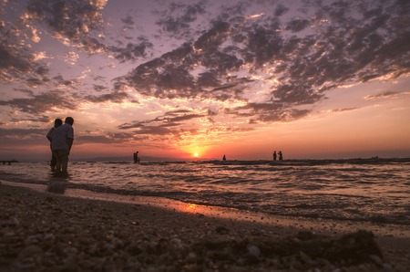 Young girls in warm water at sunset. Gorgeous colors in the sky and the sea. People standing and watching to sunset at Caspian sea. Baku, Azerbaijan. Perfect shapes reflected in waterの写真素材