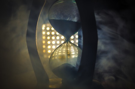Time concept. Silhouette of Hourglass clock and smoke on dark background with hot yellow orange red blue cold back lighting, or symbols of time with copy space, sandglass or sand clockの写真素材