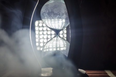 Time concept. Silhouette of Hourglass clock and smoke on dark background with hot yellow orange red blue cold back lighting, or symbols of time with copy space, sandglass or sand clockの写真素材