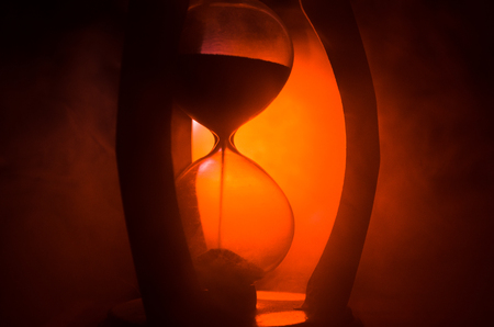 Time concept. Silhouette of Hourglass clock and smoke on dark background with hot yellow orange red...