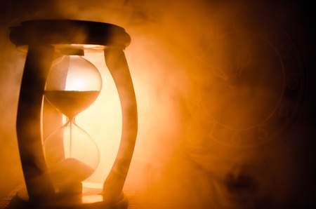 Time concept. Silhouette of Hourglass clock and smoke on dark background with hot yellow orange red blue cold back lighting, or symbols of time with copy space, sandglass or sand clockの写真素材