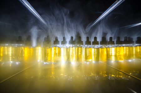Vape concept. Smoke clouds and vape liquid bottles on dark background. Light effects. Useful as background or vape advertisement or vape background.の写真素材