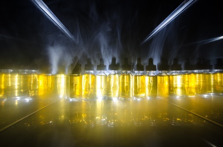 Vape concept. Smoke clouds and vape liquid bottles on dark background. Light effects. Useful as background or vape advertisement or vape background.の写真素材