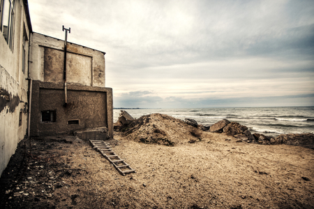 Beautiful surreal landscape of abandoned house and ladder on rocky seashore at sunset time. Cloudy weather. Caspian Sea, Azerbaijan, Novkhaniの写真素材