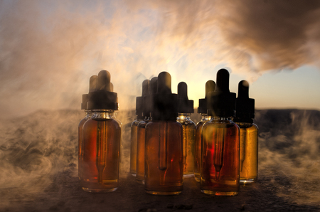 Vape concept. Smoke clouds and vape liquid bottles at sunset time. Blured background. Light effects. Useful as background or vape advertisement or vape backgroundの写真素材