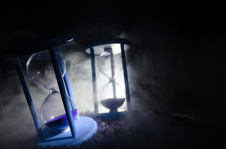 Time concept. Silhouette of Hourglass clock and smoke on dark background with hot yellow orange lighting, or symbols of time with copy space, sandglass or sand clock on chessboardの写真素材