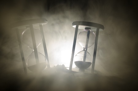 Time concept. Silhouette of Hourglass clock and smoke on dark background with hot yellow orange lighting, or symbols of time with copy space, sandglass or sand clock on chessboardの写真素材