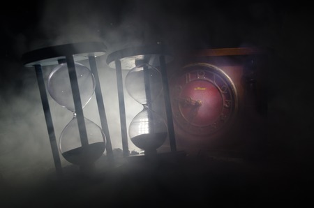 Time concept. Silhouette of Hourglass clock and smoke on dark background with hot yellow orange lighting, or symbols of time with copy space, sandglass or sand clock on chessboardの写真素材