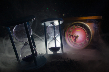 Time concept. Silhouette of Hourglass clock and smoke on dark background with hot yellow orange lighting, or symbols of time with copy space, sandglass or sand clock on chessboardの写真素材