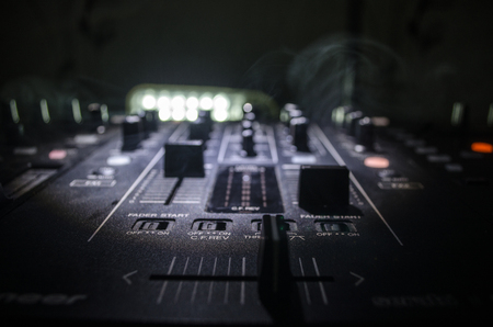 DJ Spinning, Mixing, and Scratching in a Night Club, Hands of dj tweak various track controls on dj's deck, strobe lights and fog, selective focus, close up. Dj Music club life conceptの写真素材