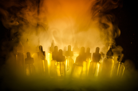 Vape concept. Smoke clouds and vape liquid bottles on dark background. Light effects. Useful as background or vape advertisement or vape background.の写真素材