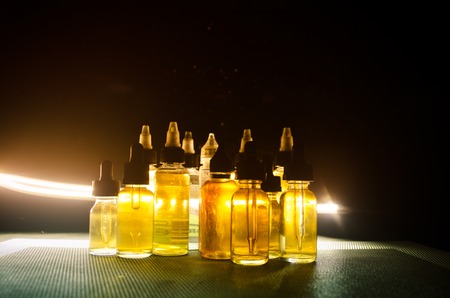 Vape concept. Smoke clouds and vape liquid bottles on dark background. Light effects. Useful as background or vape advertisement or vape background.の写真素材