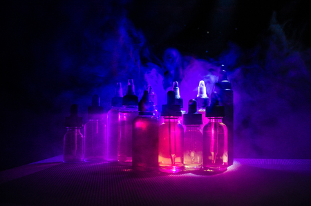 Vape concept. Smoke clouds and vape liquid bottles on dark background. Light effects. Useful as background or vape advertisement or vape background.の写真素材
