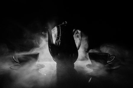 Food background tea and coffee theme. Old vintage ceramic tea or coffee pot with cups jug and sugar cup on dark background with lights and smoke. Silhouettes of ceramic tea pot and cup. Surreal decorの写真素材