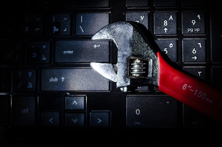 Wrench tool over a laptop on a dark background close up selective focus, repair service concept.の写真素材