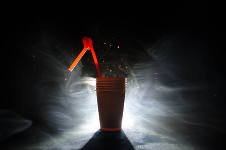 Stack of orange plastic cups with straw on dark background with smokeの写真素材