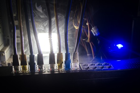 Network switch and ethernet cables, symbol of global communications. Colored network cables on dark background with lights and smoke. Selective focus. Network internet concept backgroundの写真素材