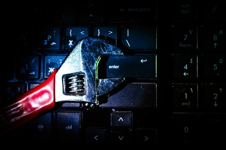 Wrench tool over a laptop on a dark background close up selective focus, repair service concept.の写真素材