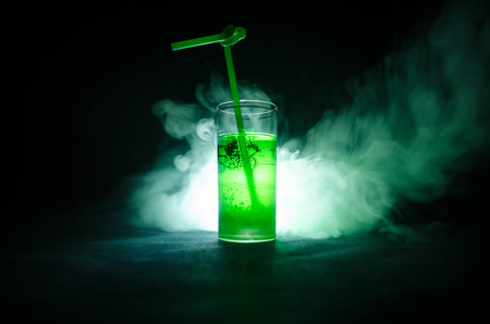 Glass of green cocktail with straw on dark background with smoke and backlights. Colorful coctailの写真素材