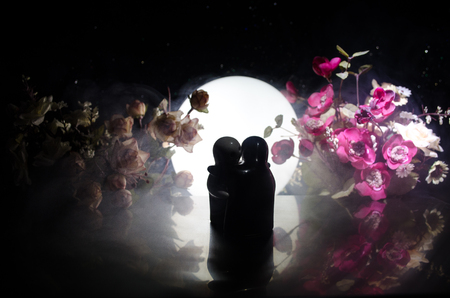 Two doll hugging on table with flowers and moon decoration Lighted background with smoke.Love concept. Greeting or gift card design idea. Silhouette of hugging coupleの写真素材