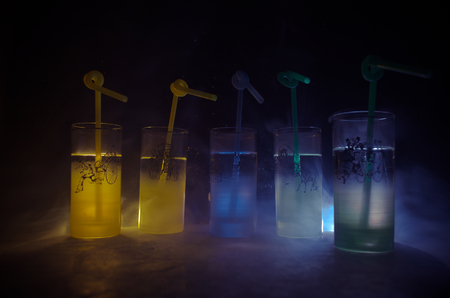 Five cocktails on the bar with smoke on dark background. Yellow, green and blue colored glasses. Club drinksの写真素材