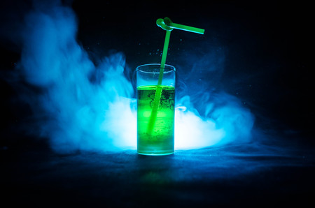 Glass of green cocktail with straw on dark background with smoke and backlights. Colorful coctailの写真素材