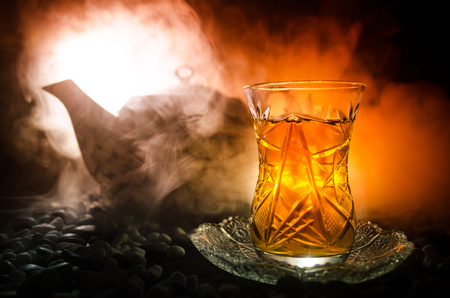 Turkish Azerbaijan tea in traditional glasse and pot on black background with lights and smoke. Eastern tea concept. Armudu traditional cupの写真素材