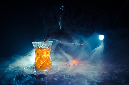 Turkish Azerbaijan tea in traditional glasse and pot on black background with lights and smoke. Eastern tea concept. Armudu traditional cupの写真素材