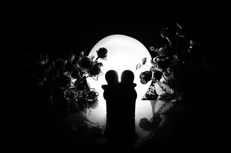 Two doll hugging on table with flowers and moon decoration Lighted background with smoke.Love concept. Greeting or gift card design idea. Silhouette of hugging coupleの写真素材