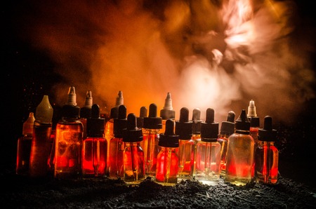 Vape concept. Smoke clouds and vape liquid bottles on dark background. Light effects. Useful as background or vape advertisement or vape background.の写真素材