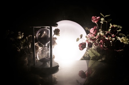 Time concept. Sand passing through the glass bulbs of an hourglass measuring the passing time as it counts down to a deadline. Silhouette of Hourglasses in smoke on dark backgroundの写真素材